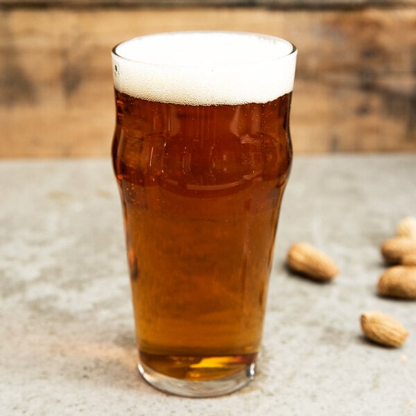 A Libbey English Pub / Nonic glass of beer on a counter with peanuts.