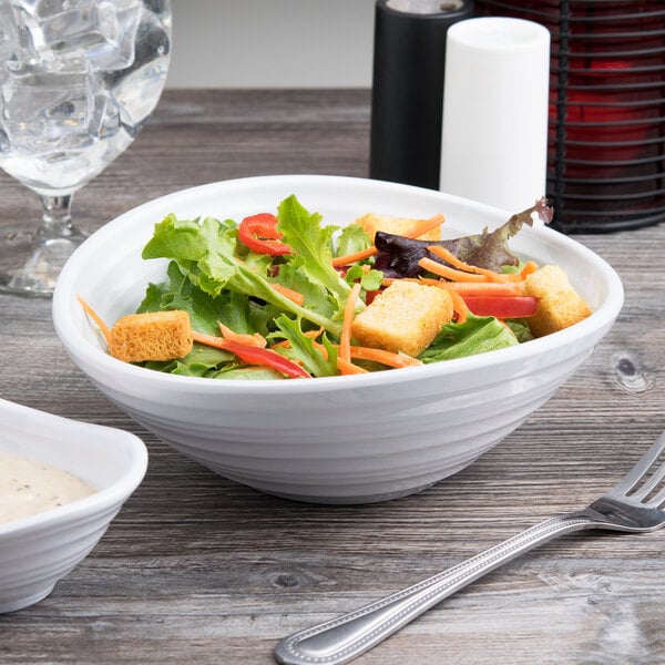 A white oblong melamine bowl filled with salad on a table.