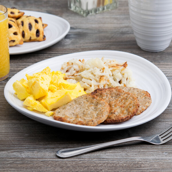 A white Elite Global Solutions melamine plate with a fork and a plate of food with eggs and sausage and a glass of orange juice.