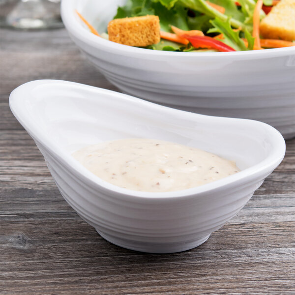A white Elite Global Solutions melamine sauce dish with white sauce in it on a white background.