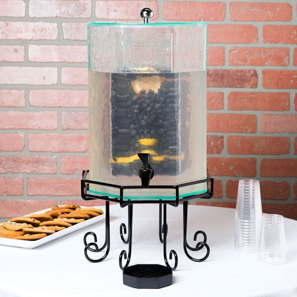 A Cal-Mil octagonal acrylic beverage dispenser with an infusion chamber on a table with cookies.