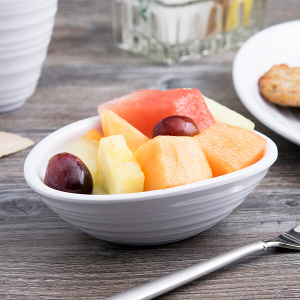 A white Elite Global Solutions oblong melamine bowl filled with fruit on a wood table.
