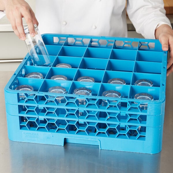 A woman using a blue Carlisle OptiClean glass rack to wash a glass bottle.