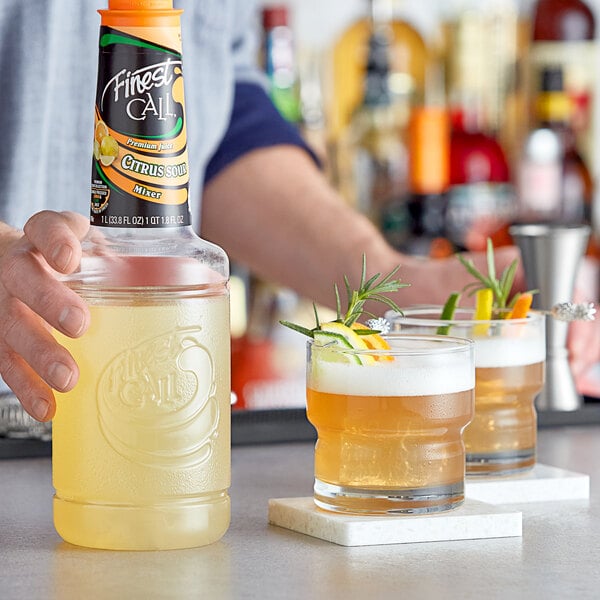 A man holding a bottle of Finest Call Premium Citrus Sour Mix next to two glasses of cocktails.