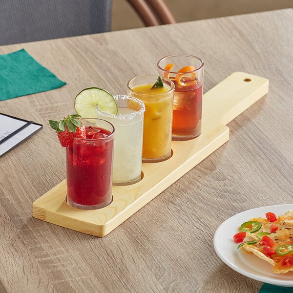 An Acopa wooden flight paddle with four Straight Up Tasting Glasses filled with drinks on a table.