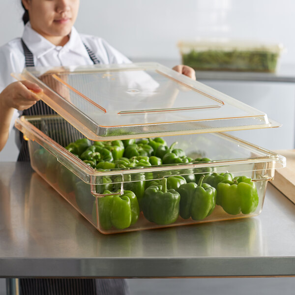 A woman holding a Cambro food storage container of green bell peppers.