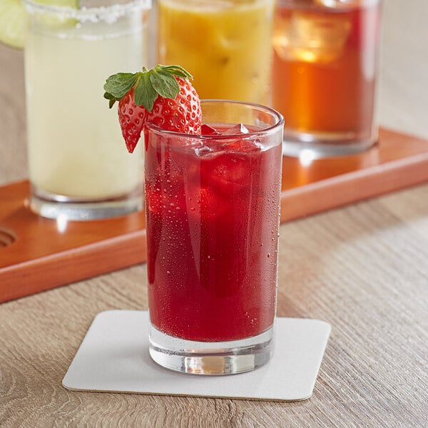 A tray with four Acopa Straight Up juice glasses filled with red liquid and ice, garnished with strawberries and a strawberry on the table.