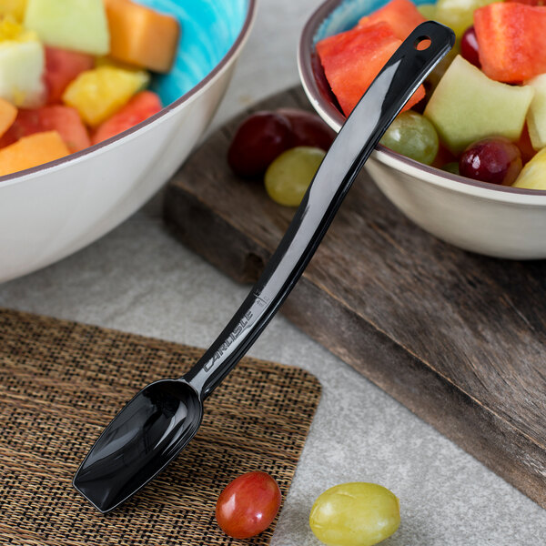 A bowl of fruit with a Carlisle black polycarbonate serving spoon.