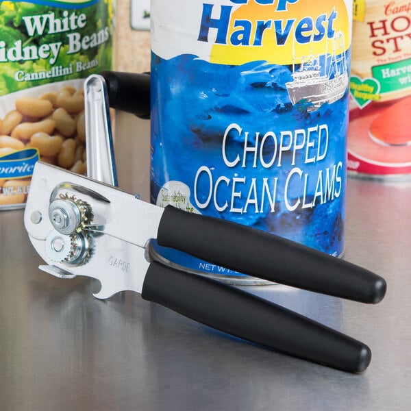 A Garde large handheld crank can opener with a black handle opening a can of chopped ocean clams on a kitchen counter.