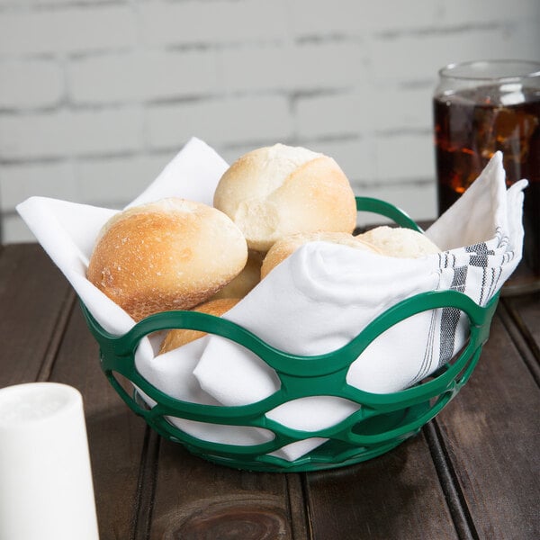 A green chili open weave basket filled with bread rolls on a table.