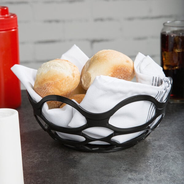 A charcoal open weave basket filled with rolls on a table with a white tablecloth.