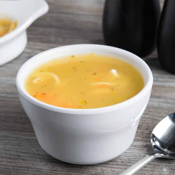 A white melamine bowl filled with soup and noodles with a spoon in it.
