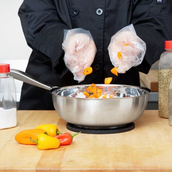 A person cooking peppers in a Vollrath stainless steel saucier pan on a counter.