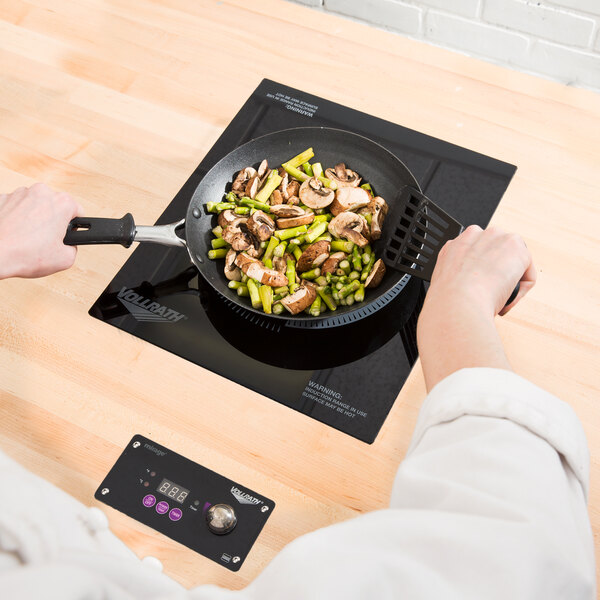 A person using a Vollrath Mirage Series drop in induction warmer to cook food in a pan on a table.