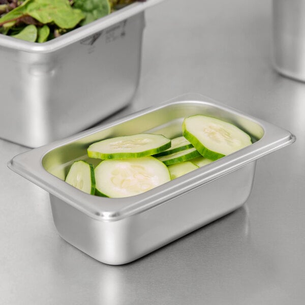 A stainless steel Choice 1/9 size steam table pan with cucumbers in it.