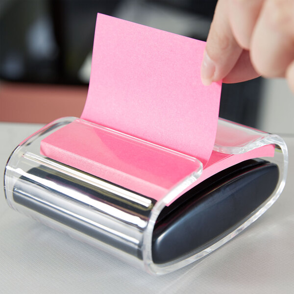 A hand putting a pink 3M Post-it note in a dispenser.