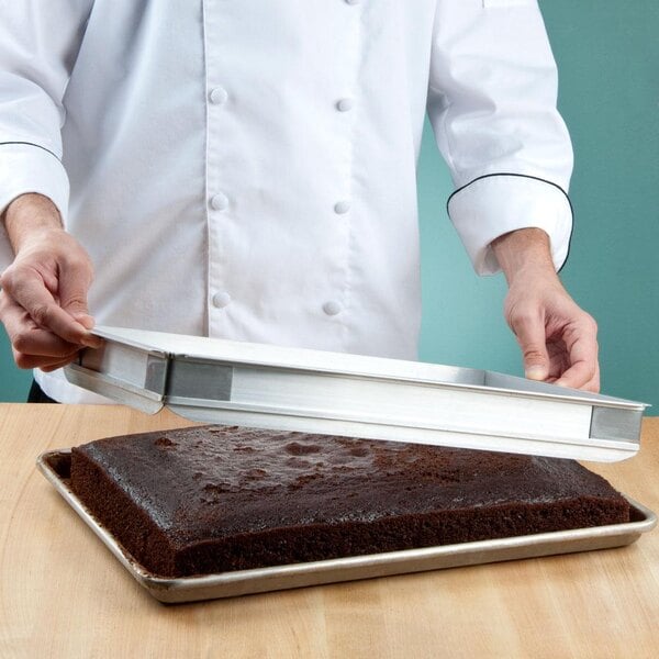 A chef holding a Baker's Mark half sheet cake pan with a chocolate cake on it.