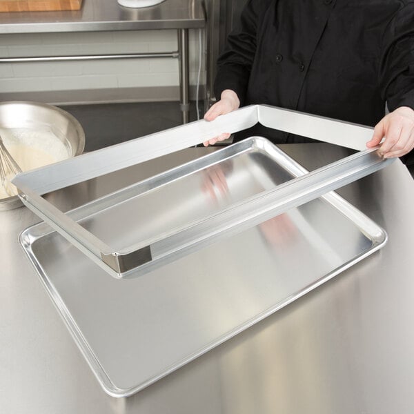 A woman using a Baker's Mark extender on a bun pan to hold a metal tray.
