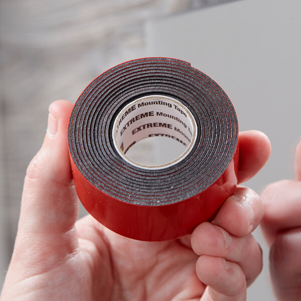 A person holding a roll of 3M Scotch black tape with black text.