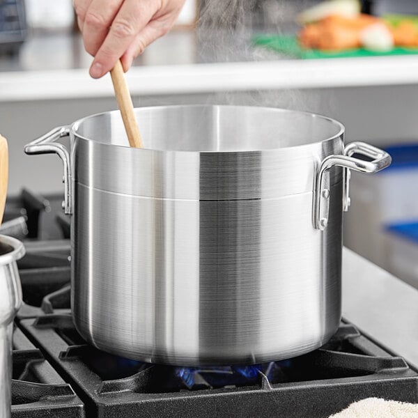 A person stirring a Choice aluminum stock pot on a stove.