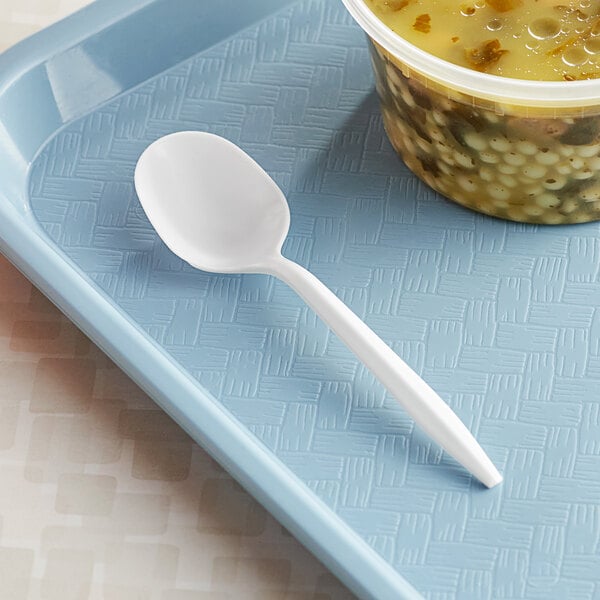 A white plastic soup spoon on a blue tray next to a bowl of soup.