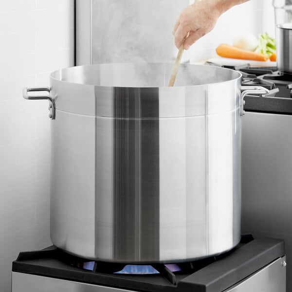 A person stirring food in a Choice aluminum stock pot on a stove.