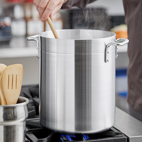 A person stirring food in a silver Choice aluminum stock pot on a stove.