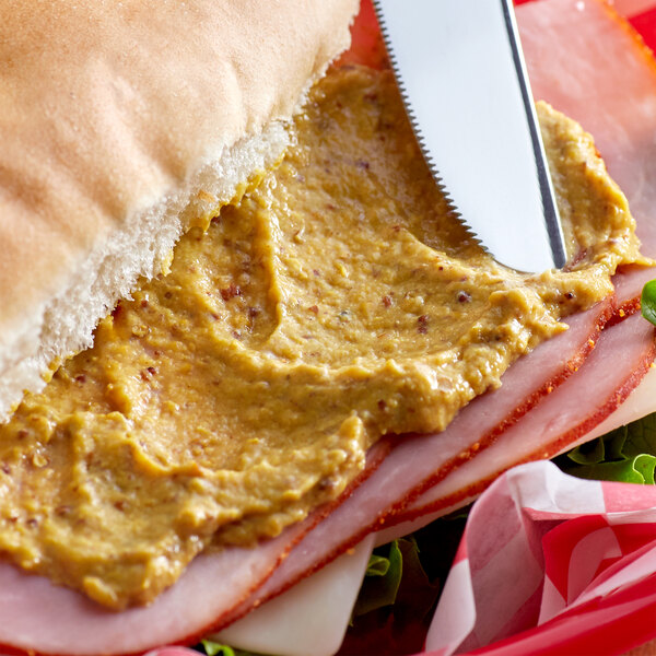 A table at a deli with a sandwich made with Admiration Deli Mustard spread on ham.