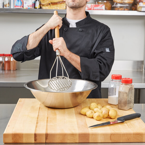 A man in a chef's uniform uses a Thunder Group Chrome Plated Potato Masher with a wood handle to mash potatoes.