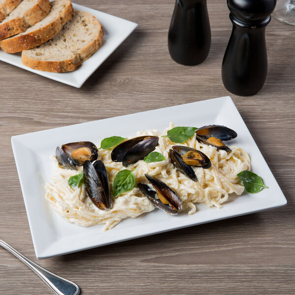 An Elite Global Solutions white rectangular melamine plate with pasta, mussels, and basil on a table.