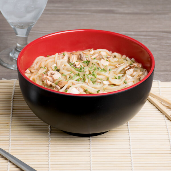 A black and red Elite Global Solutions Karma melamine bowl filled with noodles and mushrooms on a table.