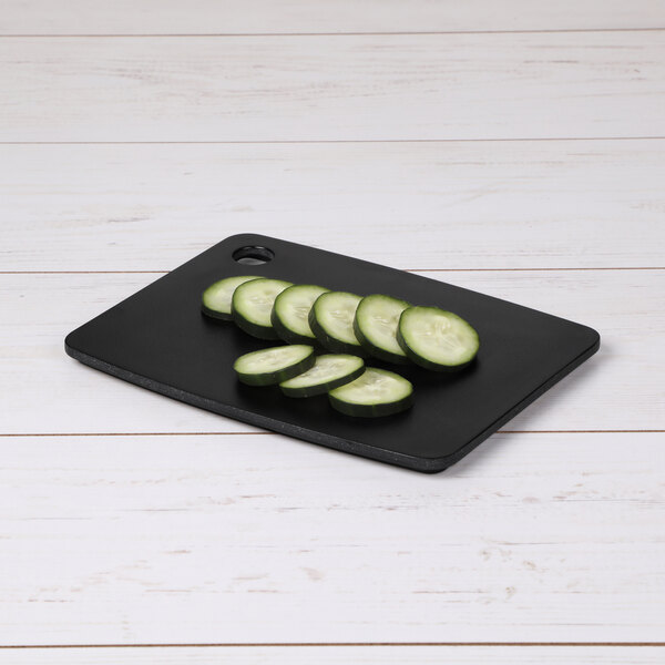 A cucumber slice on a black rectangular cutting board.