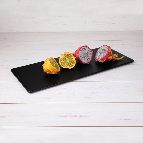 A group of cut fruit on a black rectangular serving board.
