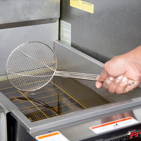 A hand holding a Thunder Group round mesh skimmer over a fryer.