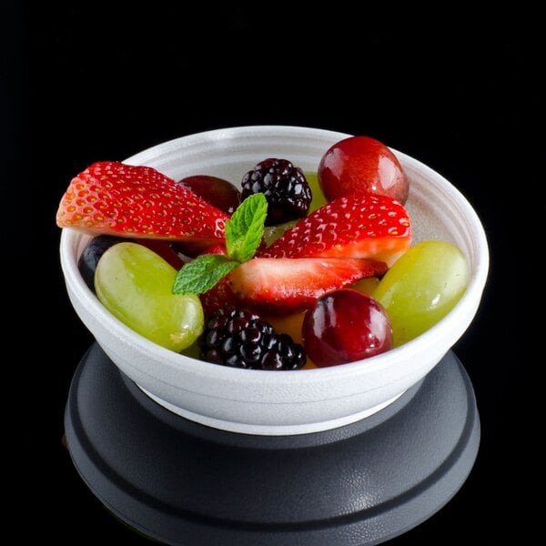 A bowl of strawberries, green grapes, and mint on a black surface in a Dart foam bowl.