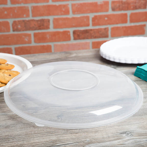 A clear Fineline plastic catering bowl lid on a table over a plate of cookies.
