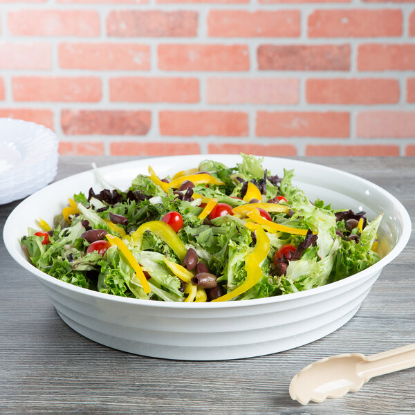 A white catering bowl filled with salad including leafy greens and yellow peppers.