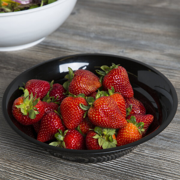 A black Fineline low profile plastic catering bowl filled with strawberries on a wooden table.