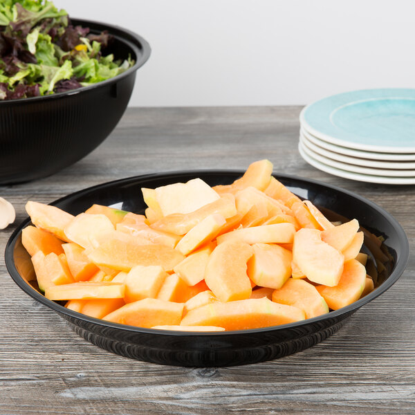 A Fineline black low profile plastic catering bowl filled with fruit and salad on a table.