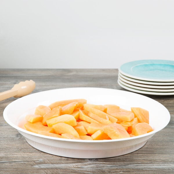 A white Fineline low profile plastic catering bowl filled with cut up fruit on a table.