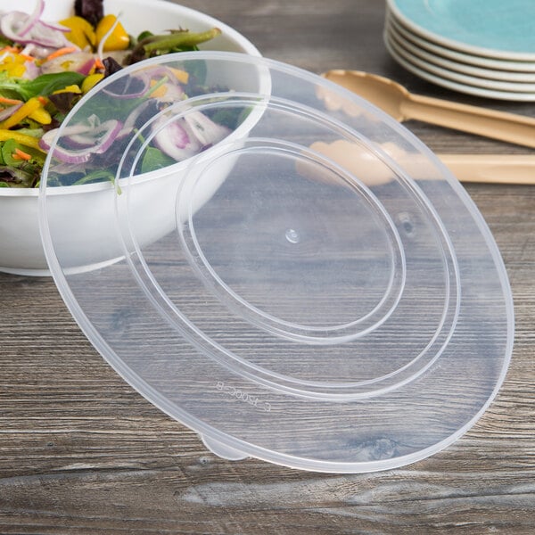 A clear plastic catering bowl with a lid on top filled with salad.