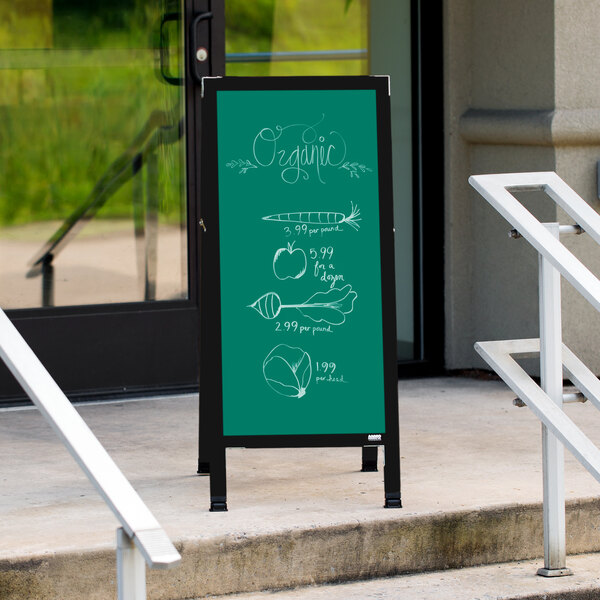 A black Aarco A-Frame chalkboard sign with green writing on the sidewalk.