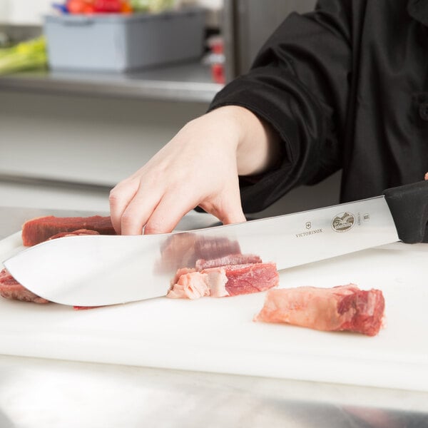 A person cutting meat with a Victorinox Butcher Knife on a cutting board.