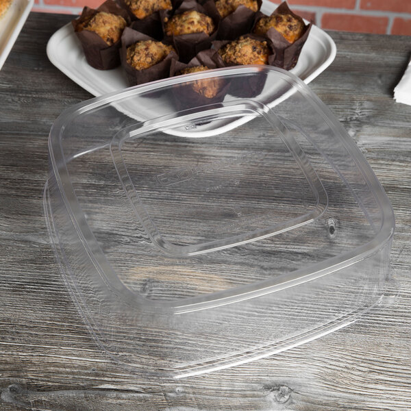 A clear plastic container with a Eco-Products Regalia clear plastic lid on a plate with muffins.