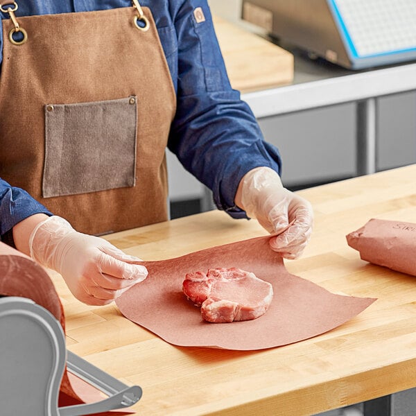 A person in a brown apron cutting meat on a table.