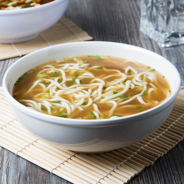A close up of a Thunder Group ivory melamine pho noodle bowl filled with soup and noodles.