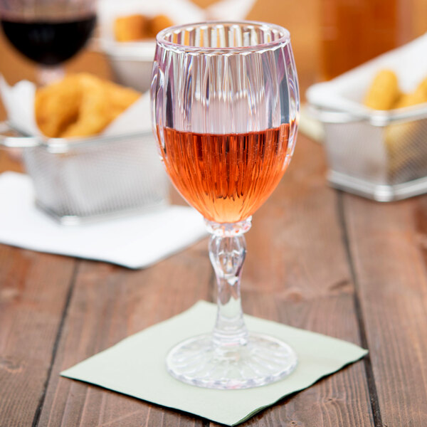 A customizable fluted wine glass filled with pink liquid on a table with food.