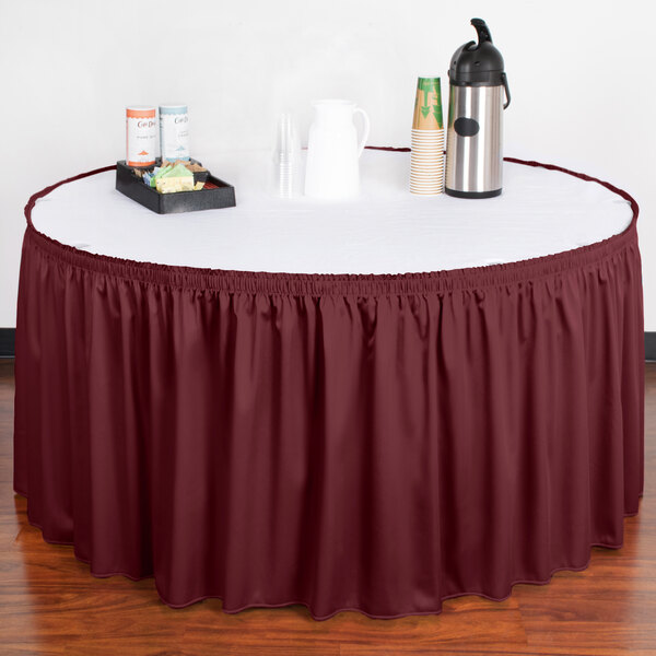 A table with a white table cloth and a burgundy shirred pleat table skirt with velcro clips on a table.