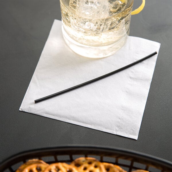 A black Eco-Products compostable plastic cocktail straw in a glass of water on a napkin.