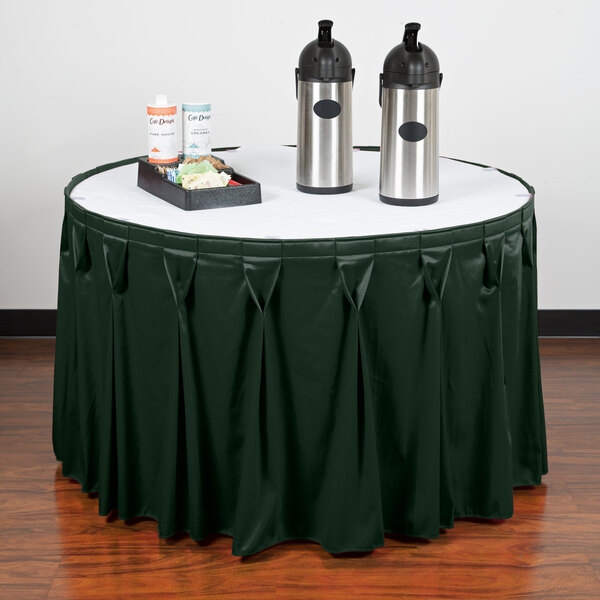 A table with a Snap Drape Wyndham jade green bow tie pleat table skirt and two bottles of liquid on it.